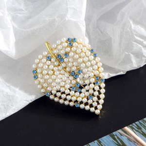 Golden leaf brooch featuring white pearls and blue rhinestones on a textured background