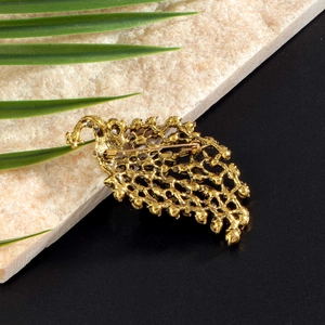 Reverse side of golden peacock brooch showing safety pin clasp and hollow metalwork