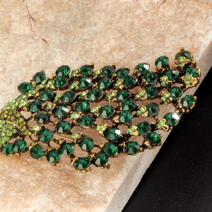 Elegant gold peacock brooch featuring layered green crystals and sparkling rhinestones