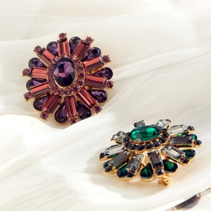 Elegant floral brooches with purple and green crystals on white satin background