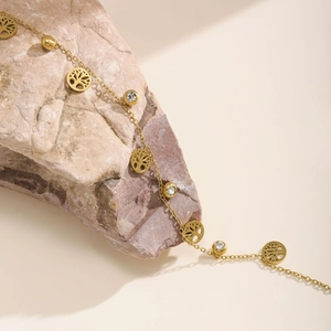 Golden Tree of Life anklet with white zircon beads on a textured natural stone background