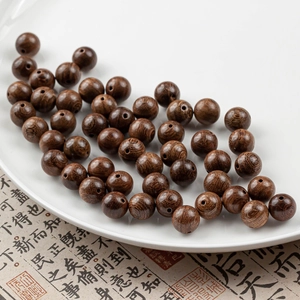 Macro detail of 10mm dark brown sandalwood beads with natural grain on white ceramic tray