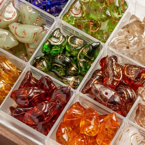 Assorted colorful glass bird beads with gold accents in a transparent storage box