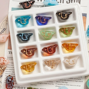 Close-up of bird-shaped Czech glass beads with gold lining in a white sorting tray
