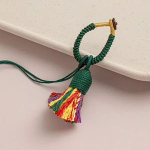 Handmade green knot pendant with colorful tassels on a decorative ceramic tray