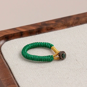 Macro detail of green braided rope keychain with gold wire and wooden button closure