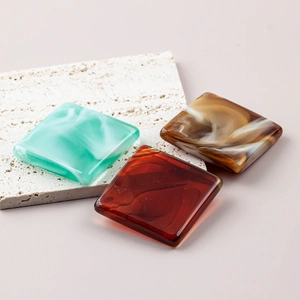 Close-up of polished resin square beads with faux marble and amber textures on travertine