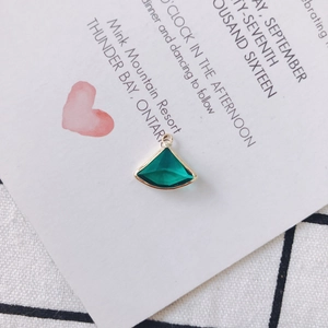 Detail of fan-shaped emerald green crystal pendant with gold alloy trim on display card