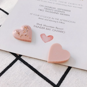Detailed macro view of pink resin heart pendants with gold foil on a wedding card