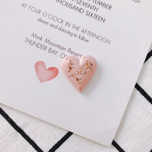 Macro detail of pink resin heart earring with embedded gold flakes on white card