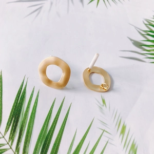Makro-Detail von unregelmäßigen mattgoldenen Ohrsteckern mit gewelltem Randdesign