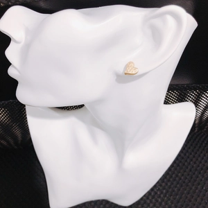 Macro detail of golden heart stud earrings with unique hammered dot texture on model