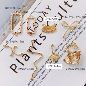 Macro-opname van diverse gouden DIY-sieradenhangers met ginkgobladeren en geometrische kaders