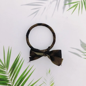 Close-up of a camouflage print hair tie with a bow knot on a summer tropical leaf background