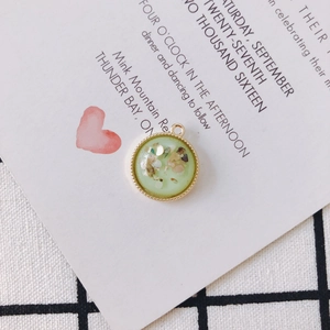 Close-up of a light green resin pendant with colorful flakes and golden beaded edge