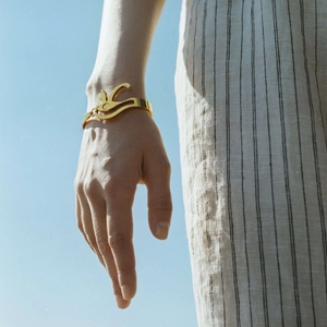 Bracciale dorato occhio del male con design astratto indossato su sfondo di cielo blu