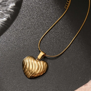 Collier cœur doré poli avec texture ondulée sur une surface noire élégante