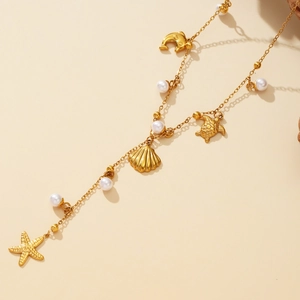 Collier de perles doré avec étoiles de mer et coquillages sur fond beige neutre