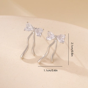 Macro detail of bow-shaped stud earrings with zircon hearts and metal ribbons