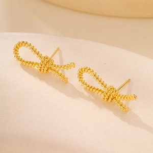 Detail of gold knot earrings with twisted spiral texture on a beige minimalist background