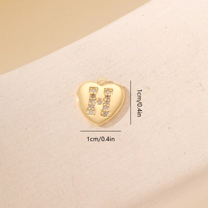 Primo piano di un ciondolo a cuore dorato con lettera H in zircone su pietra