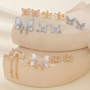 Gold and silver butterfly stud earrings with sparkling crystals on beige geometric stands
