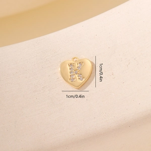 Macro di ciondolo a cuore dorato con lettera K in zircone su sfondo beige materico
