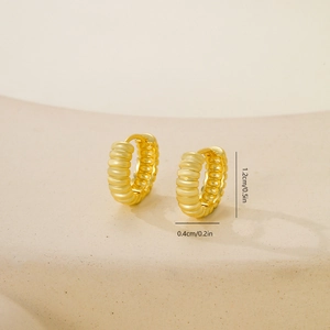 Vista macro de pendientes huggie dorados con textura espiral sobre piedra