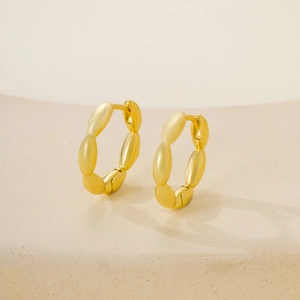 Pendientes de aro geométricos dorados minimalistas sobre un elegante pedestal blanco roto