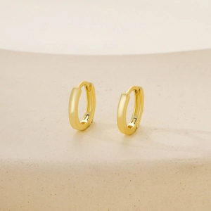 Minimalist glossy gold round hoop earrings with hidden clasp on a beige pedestal