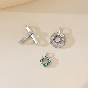 Three minimalist silver pendants with zircon heart, star, and cross designs on beige background