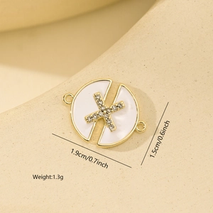Macro shot of a gold-plated round pendant with rhinestone X and white enamel