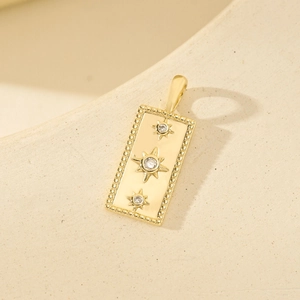 Gold square pendant with zircon star pattern and milgrain edge on sandstone background