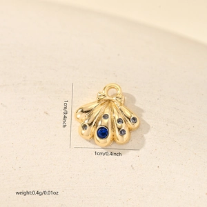 Macro detail of gold shell charm with blue stone, bow element and 1cm size mark