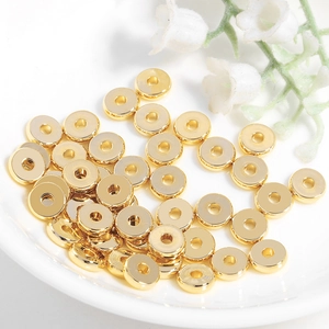 Cuentas espaciadoras planas de latón dorado para joyería DIY en un plato de cerámica blanca