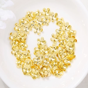 Goldene Blumen-Perlenkappen und Metall-Abstandshalter für DIY-Schmuck auf weißer Keramik