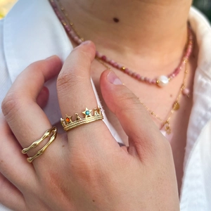 Close-up of a gold-plated crown ring with colorful zircons and a wavy double-layered ring