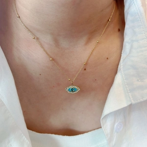 Collar de Ojo Turco dorado con cristales azules y cadena de cuentas en camisa blanca