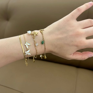 Gold layered bracelet set featuring butterfly charms, pearls, and green gemstone pendants
