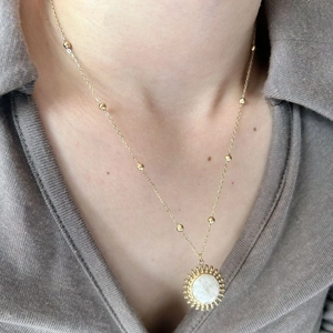 Collier à pendentif soleil doré avec pierre blanche et chaîne perlée sur un mannequin
