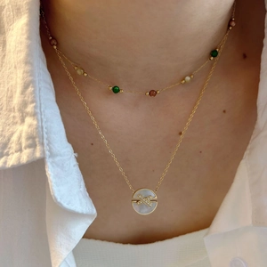 Layered gold necklace featuring colorful beads and a round shell pendant with pavé diamonds