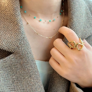 Double layered gold necklace with turquoise beads worn on a brown herringbone blazer