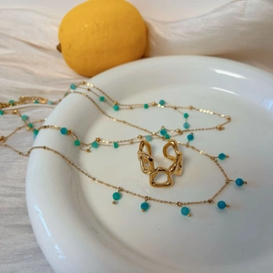 Layered gold necklace with amazonite beads and geometric hollow ring on white silk