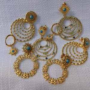 Elegant gold-tone earrings with blue stones and multi-layered rings on white fabric