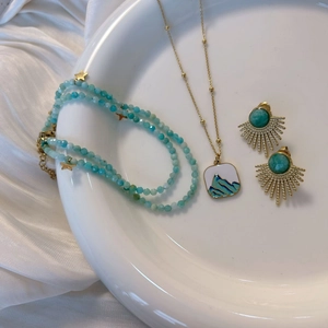 Juego de joyas de amazonita con aretes de sol dorados y collar de cuentas azules en plato
