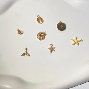 Goldene Meeres-Anhänger mit Seestern, Muschel und Meerjungfrauenschwanz auf weißem Tablett
