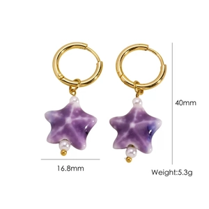 Detail view of gold hoop earrings with purple ceramic star charm and white pearl accents