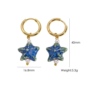 Detail shot of star-shaped earrings with blue-green ceramic and pearl in gold finish