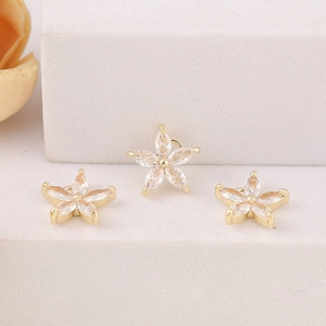 Trois pendentifs fleur en or avec zircons taille marquise sur un fond crème texturé