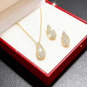 Detalle de conjunto de joyas de gota dorada con circonitas en una caja de regalo roja